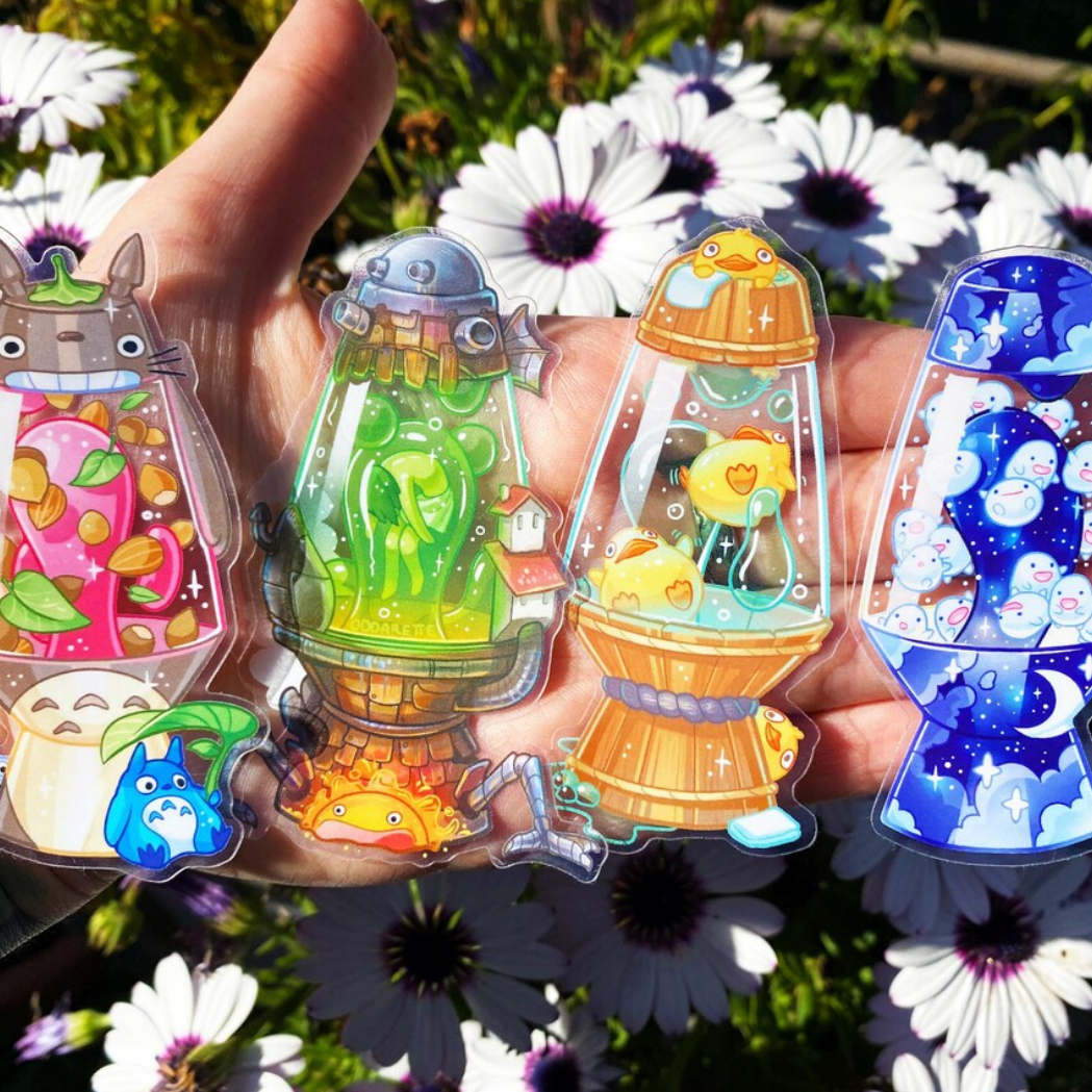 Four lava lamp sticker printed in colorful, bright colors on transparent, with playful, cute characters, held against a flower bed.