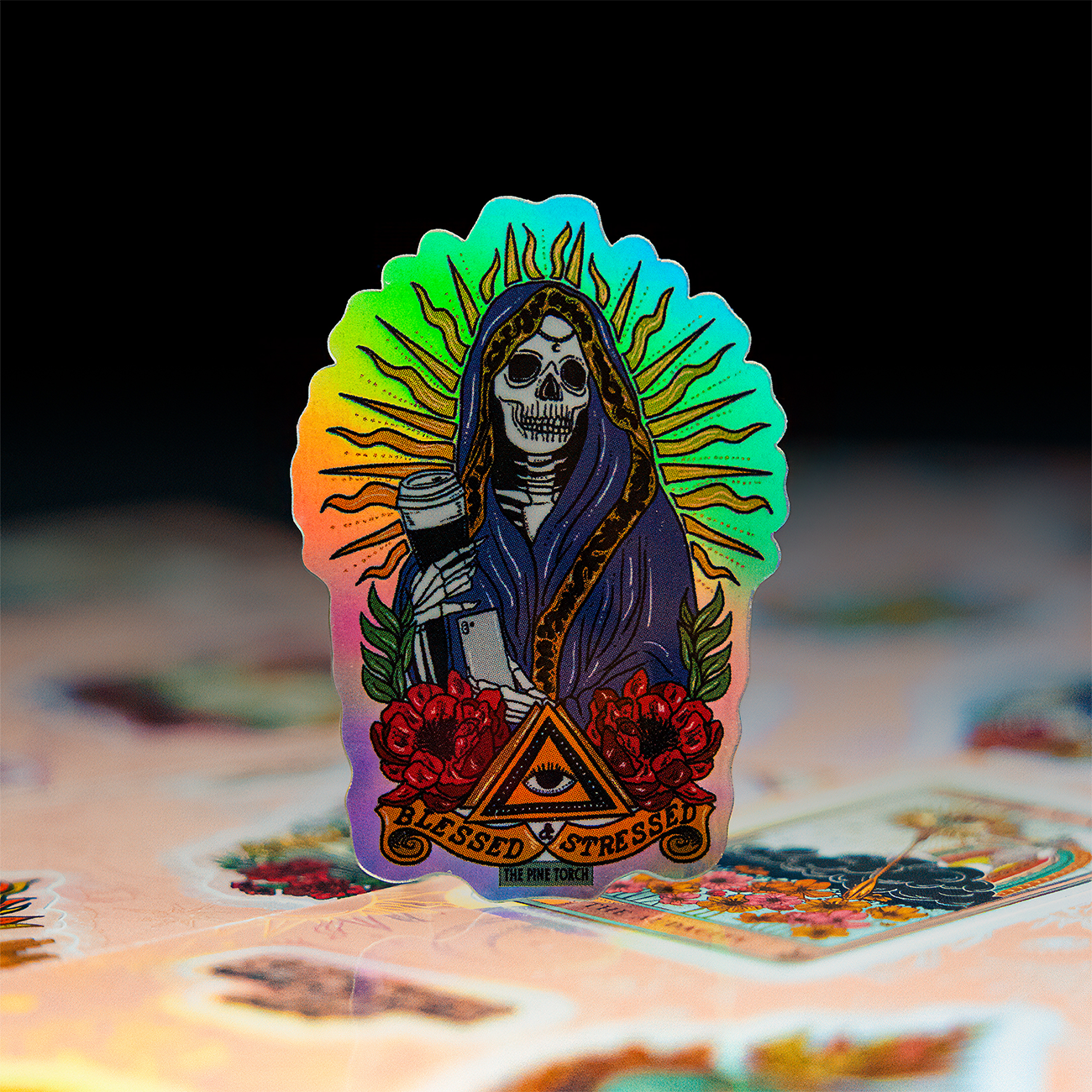 Holographic skull design printed on a sticker sheet with the text "Blessed and Stressed" on top of sticker sheets against a dark background.