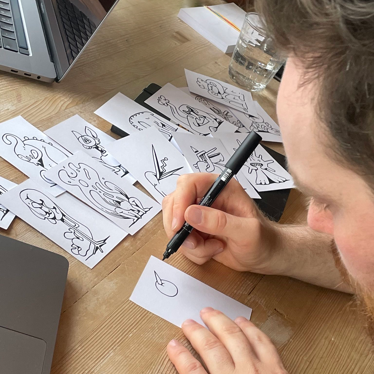 Daniel Harisberger sketching characters with a black pen on white paper slips, in a studio.