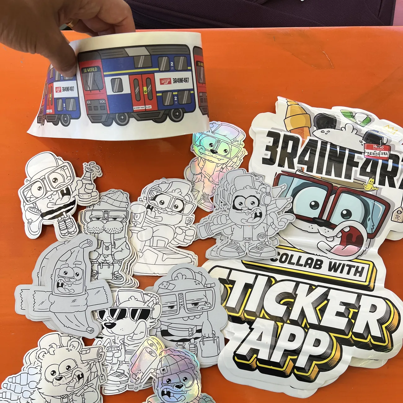 Etikett med S8 World-tåget från Brainfart x StickerApp med skylten "In every fart is art", som hålls upp ovanför svartvita die-cut klistermärken