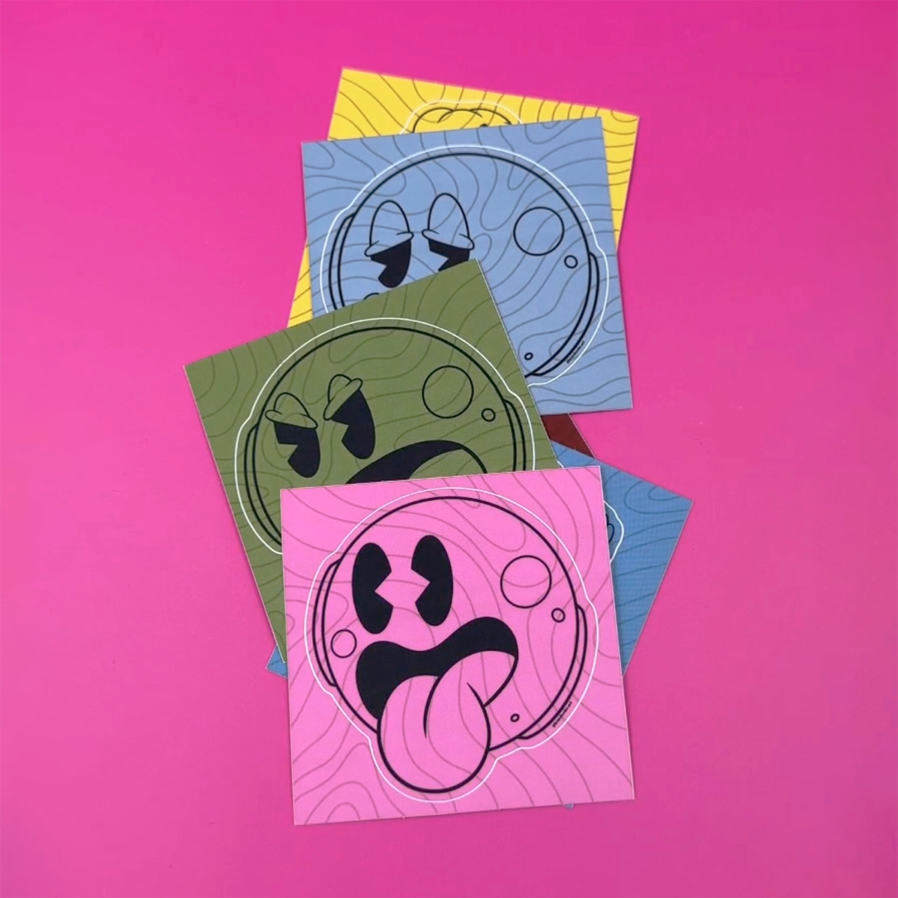 Kiss-cut klistermärken med smiley-ansikten i olika färger och ansiktsuttryck tryckta på matt vinyl, mot en rosa bakgrund.