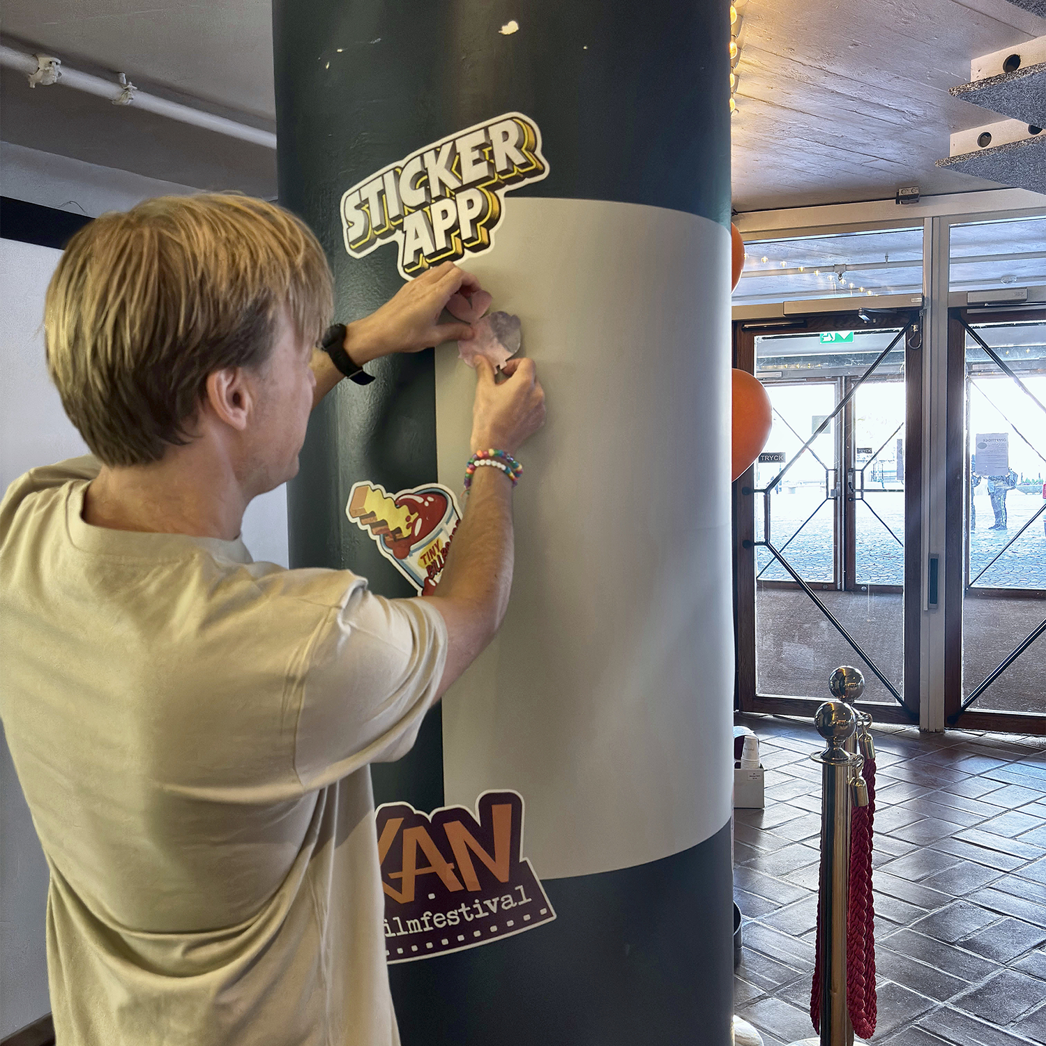 Man som sätter upp ett klistermärke på StickerApps klistermärkesvägg runt en pelare på KAN filmfestival