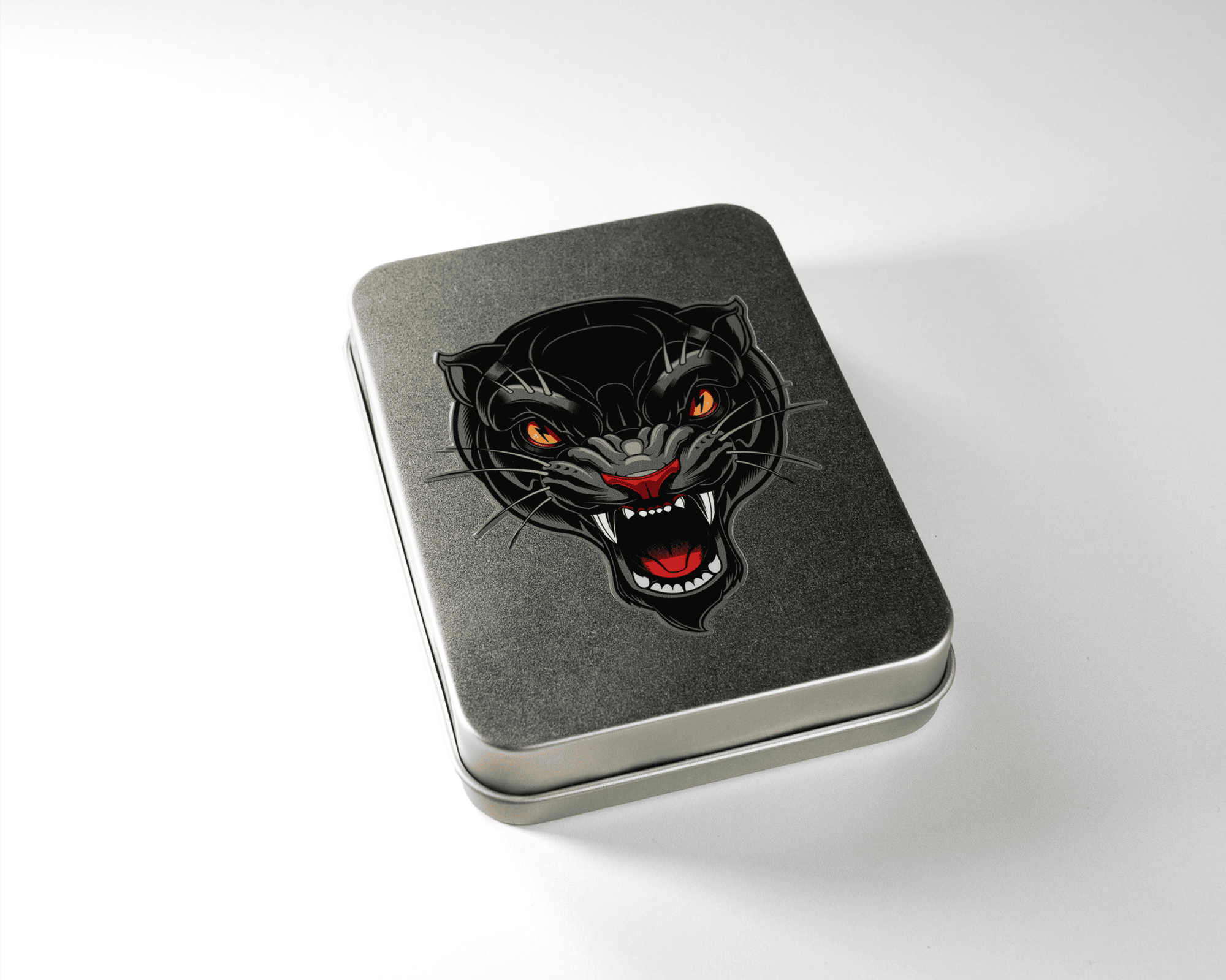 A metal tin with a black panther uv dtf sticker on the lid, featuring glowing orange eyes and an open mouth, placed on a white surface.
