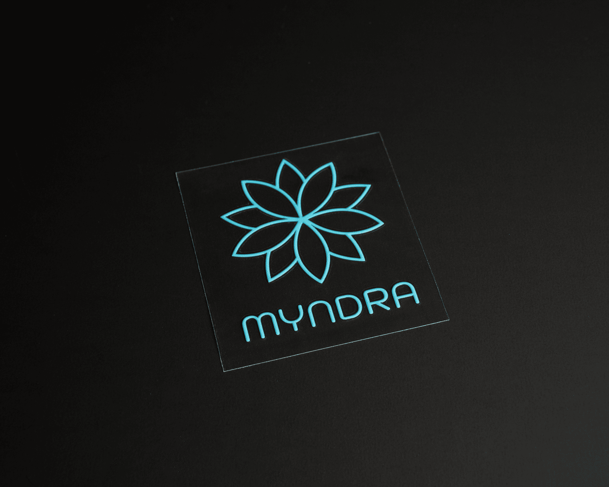 En turkos geometrisk blomma logotyp UV DTF transfer klistermärke med ordet "MYNDRA".