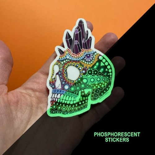 A hand holding a glow in the dark sticker with a skull on it