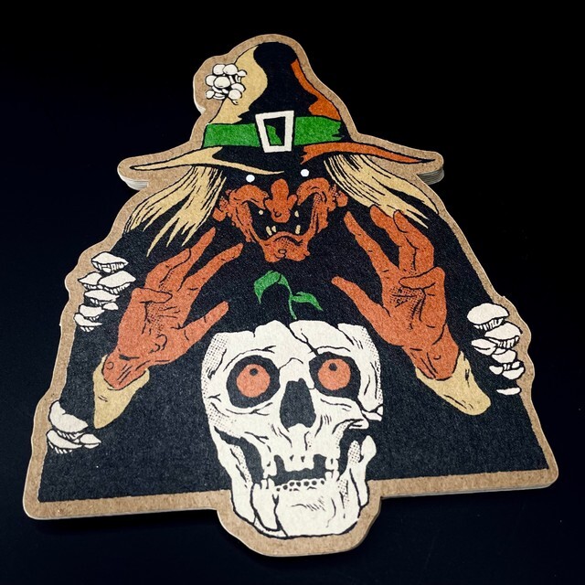 A die cut kraft paper sticker of a skull with a witches hat on it