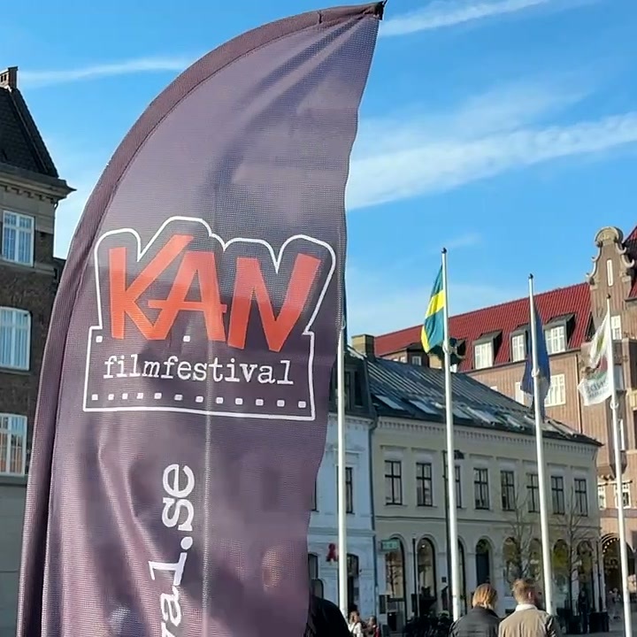 Beachflagga för KAN filmfestival framför historiska byggnader och flaggor på ett torg i Lund